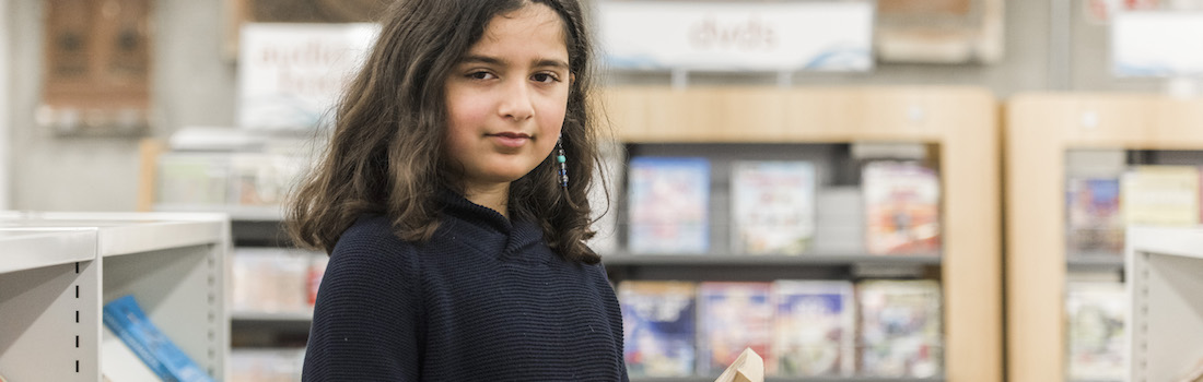 Image of young girl beside shelves of library books